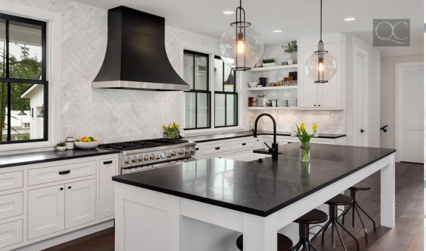 Beautiful Kitchen in New Luxury Home. Features Black Counters and Island, with White Woodwork and Cabinetry. Lights are Turned On.