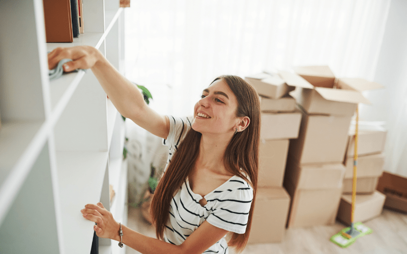 female pro organizer wiping down shelf with cloth, with packing boxes behind her