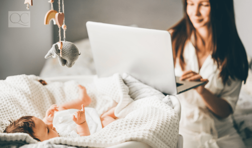 mother on laptop while baby lies in crib