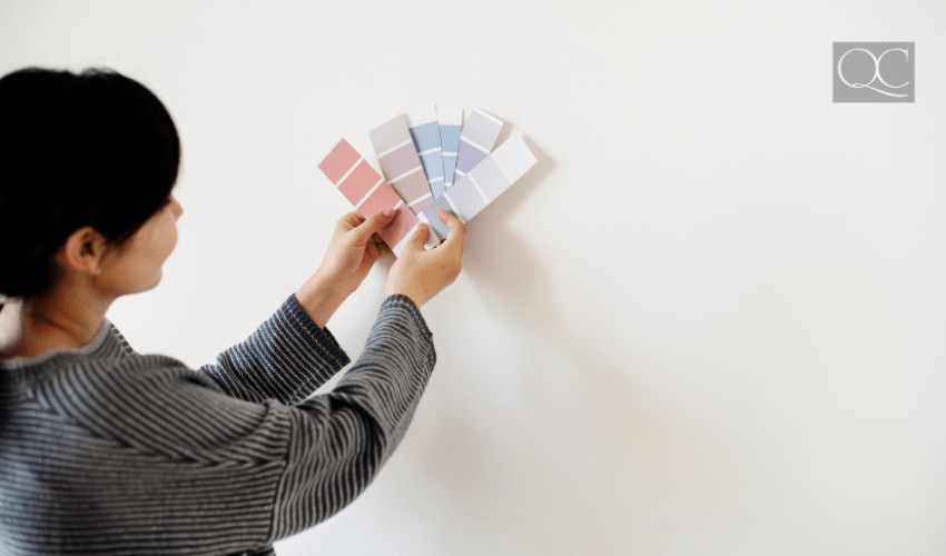 woman holding up paint color swatches to white wall