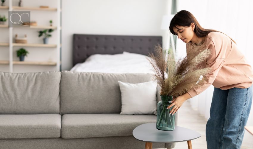 Casual young lady putting glass vase with dried flowers on tea table. Millennial woman decorating her modern apartment and bedroom or living room with pampas grass