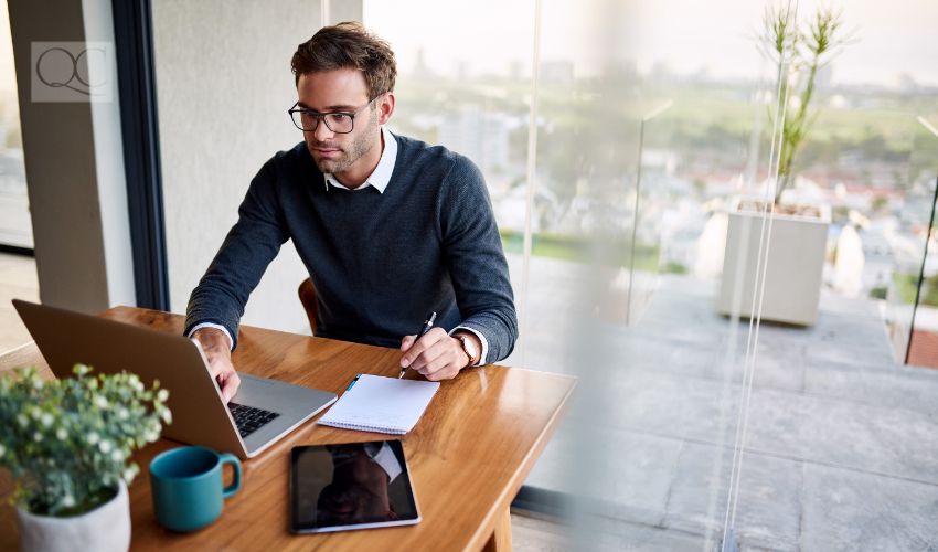 Young businessman sitting at a table at home working on a laptop and writing down ideas in a notebook