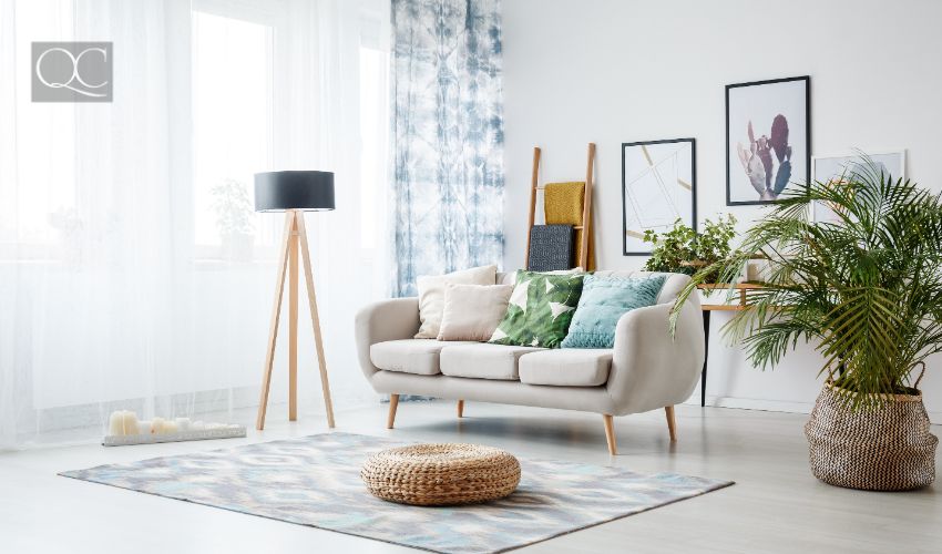 Black lamp standing by a sofa and a row of candles lying on the floor in front of a window shedding light on the interior of boho style living room