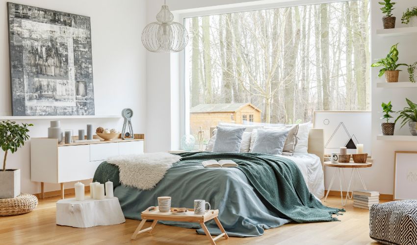 Green and blue bedsheets on bed in bedroom interior with painting on the wall and window