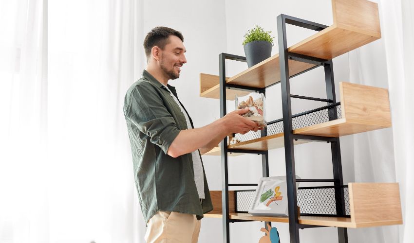 home improvement and decoration and people concept - happy smiling man placing seashells in vase to shelf