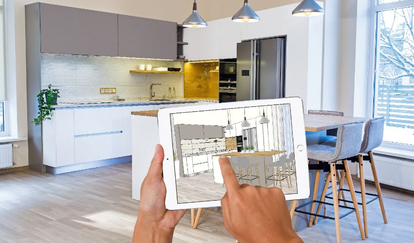 Hands holding tablet with kitchen interior sketch. In background real finished kitchen interior design. Kitchen presentation. Dinning table. Home Interior Design Software Programs.Project management. Interior design business article.