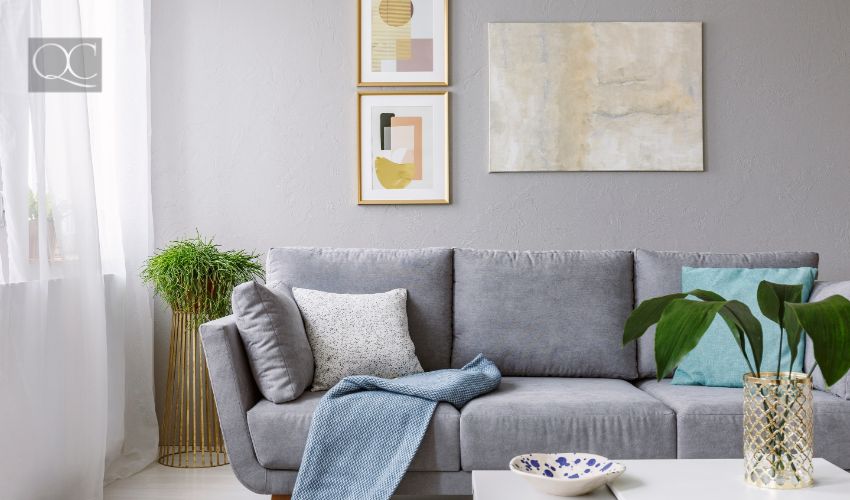 Real photo of a grey sofa standing in a stylish living room interior behind a white table with leaves and in front of a grey wall with posters, interior decorating client